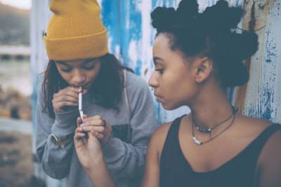 Afro teen lighting her grungy girl friend's cigarette with another cigarette